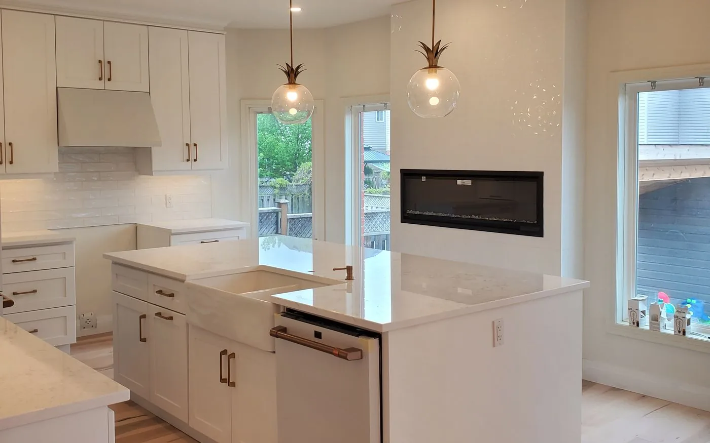 White custom kitchen with a quartz island, farmhouse sink, glass pendants and a linear fireplace