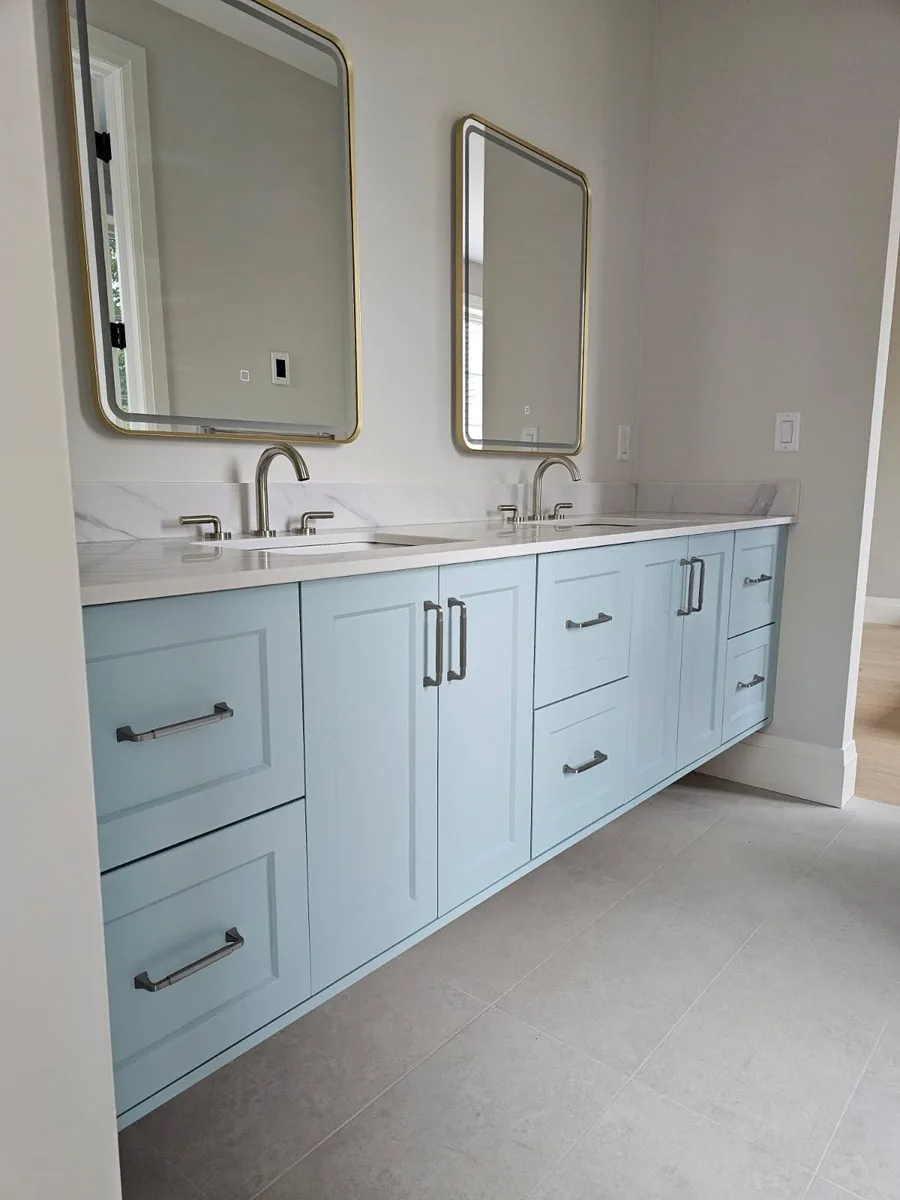 Double vanity bathroom with soft blue shaker cabinetry, quartz top and twin framed mirrors
