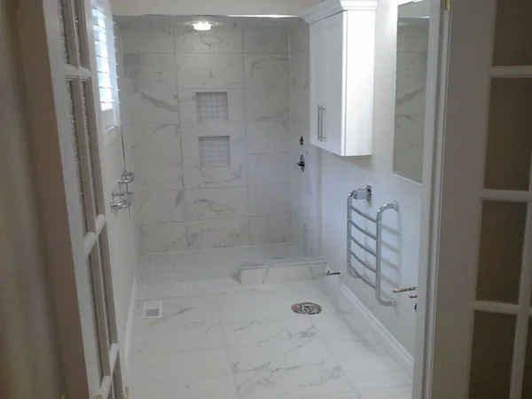 Curbless marble tiled shower with a bench, niche and a linear drain