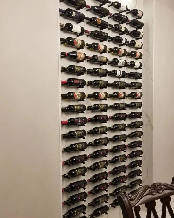 Floor to ceiling wine wall with metal peg racking holding several dozen bottles