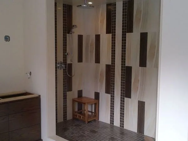 Walk in shower with a vertical feature tile stripe and a teak bench